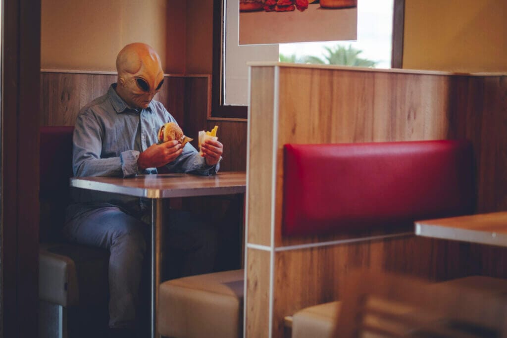 Hombre con máscara de alienígena sentado solo en una cafetería