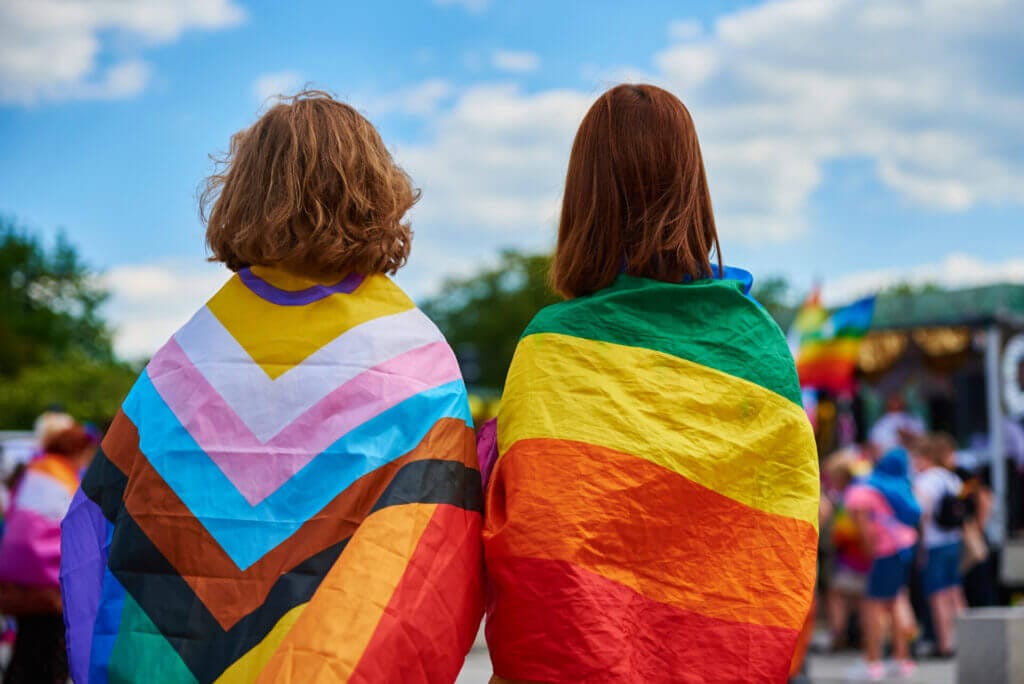 Dos mujeres de espaldas con las banderas del orgullo LGBTQ+ en sus hombros