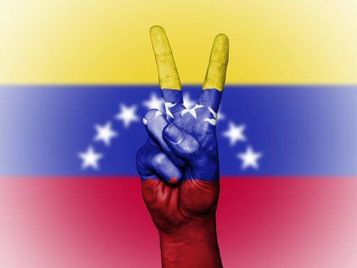 Mano haciendo el símbolo de la paz sobre una bandera de Venezuela - Este artículo habla sobre una coalición de venezolanos en Estados Unidos que demanda la ciudadanía para Dreamers, TPS y campesinos.
