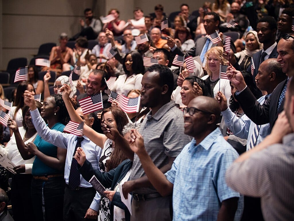 Este artículo habla sobre la nueva regla de carga pública. La foto muestra muchas personas con banderines de los Estados Unidos.