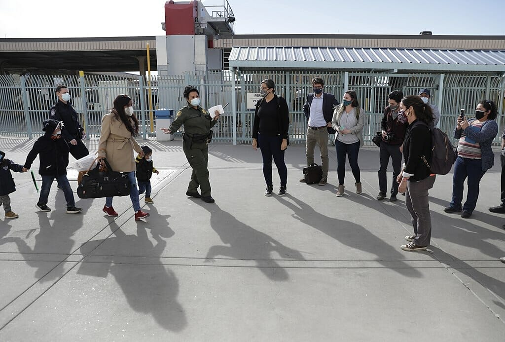 Este artículo habla sobre la demanda por la terminación de Título 42. La imagen muestra un grupo de solicitantes de asilo siendo procesados administrativamente en la frontera.