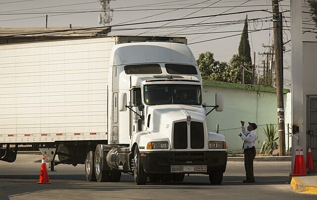 Este artículo habla sobre el bloqueo en la frontera. La imagen muestra a un camión comercial junto a un oficial de BPS.