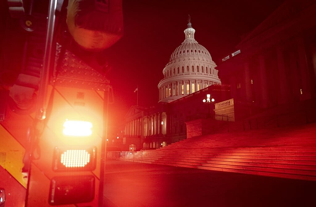 Este artículo habla sobre la teoría conspirativa del Gran Reemplazo. La imagen muestra al Capitolio de los Estados Unidos iluminado con luz roja de un vehículo en la noche del 6 de Enero de 2021.