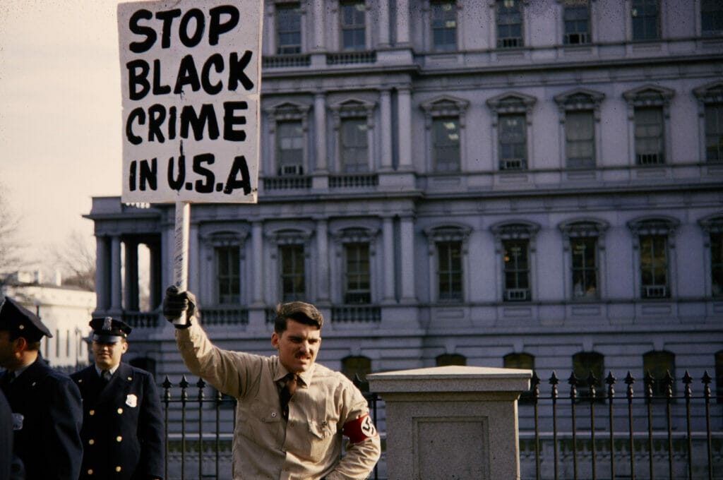 Este artículo habla sobre la teoría conspirativa del Gran Reemplazo. La imagen es una foto histórica del archivo del National Park Service de un Nazi protestando en el Capitolio en 1965.