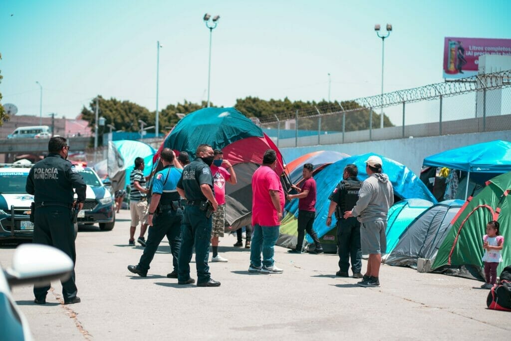 Este artículo habla sobre los migrantes que aguardan del lado mexicano para cruzar la frontera. La imagen muestra un campamento de migrantes en Tijuana.