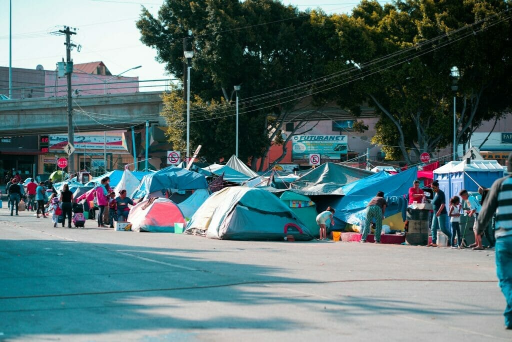 Este artículo habla sobre los migrantes que aguardan del lado mexicano para cruzar la frontera. La imagen muestra un campamento de migrantes en Tijuana.