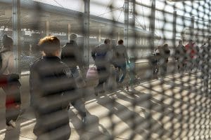 Este artículo habla sobre el fin del programa Quédate en México. La imagen muestra un grupo de solicitantes de asilo haciendo fila para ingresar a Estados Unidos. La fotografía está tomada a través de una reja.