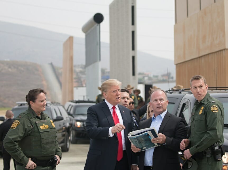 Este artículo habla sobre la separación de familias migrantes. La imagen muestra al ex presidente Donald Trump en la frontera observando prototipos para el muro fronterizo.