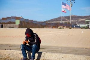 Este artículo habla sobre la expulsión de migrantes en la frontera. La imagen muestra a un hombre sentado con el muro fronterizo de fondo.