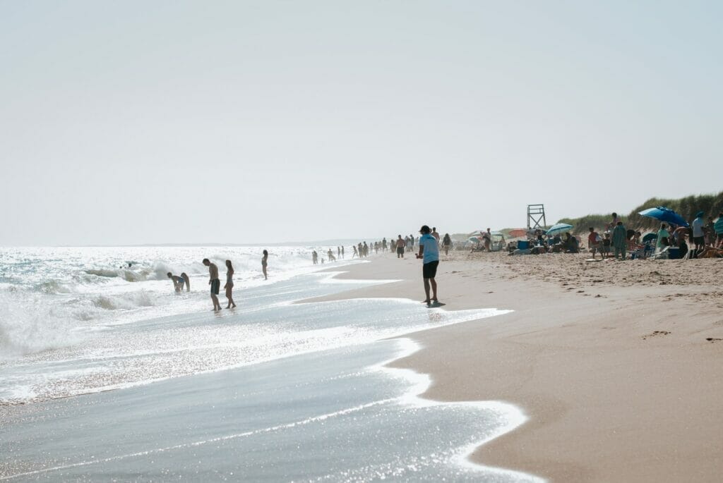 Playa de Martha's Vineyard. Algunas personas mojan sus pies en el agua y otras están ubicadas bajo sombrillas.