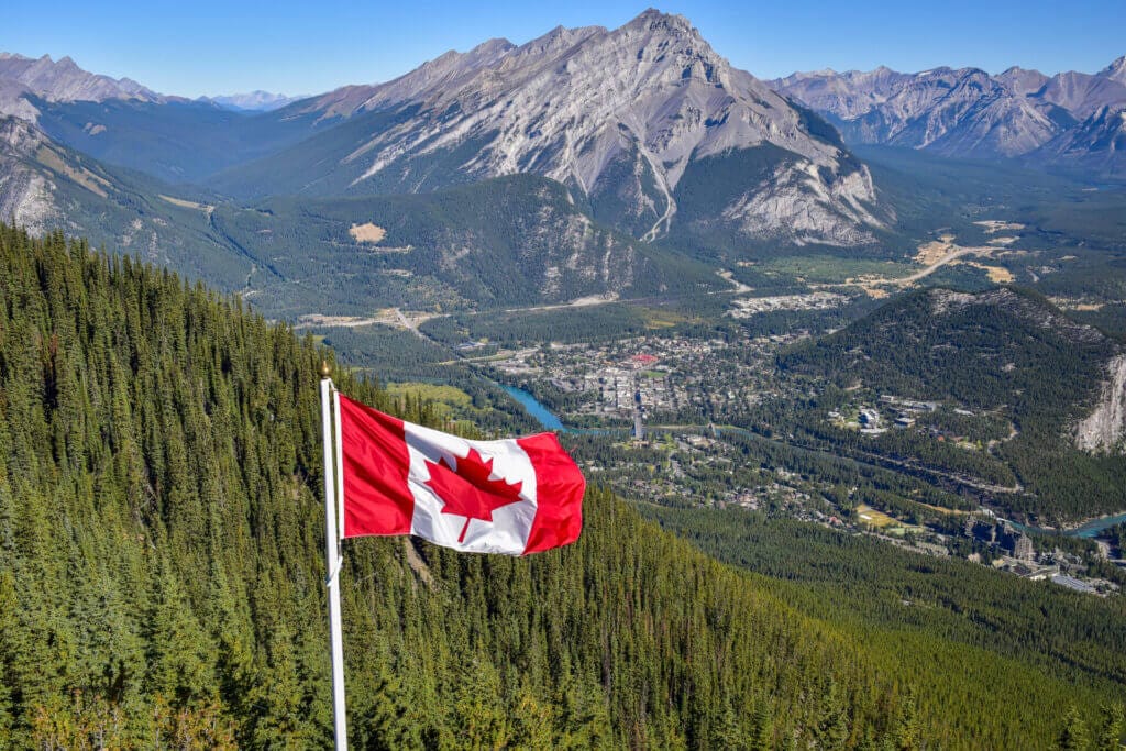 Bandera de Canadá ondeando sobre las Montañas Rocosas. Este artículo habla sobre emigrar a Canadá.