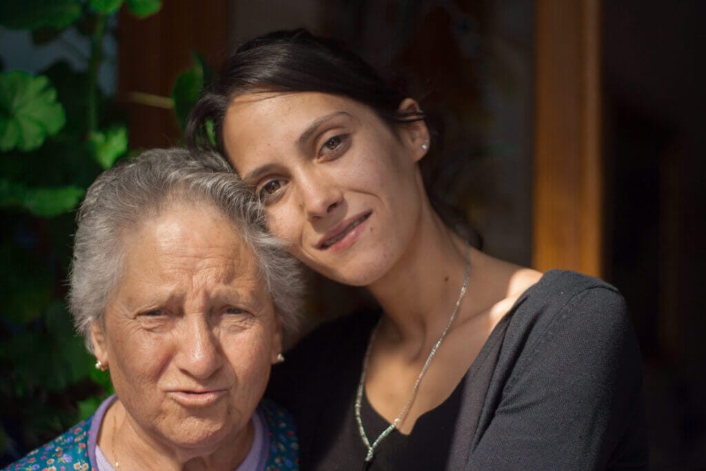 Una mujer mayor junto a una mujer joven, ambas de ascendencia latina. Este artículo explica qué es el perdón migratorio y cómo conseguirlo.