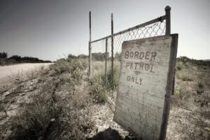 Muro de reja en la frontera entre Estados Unidos y México. Un cartel de madera indica que el camino es exclusivo para la Patrulla Fronteriza.