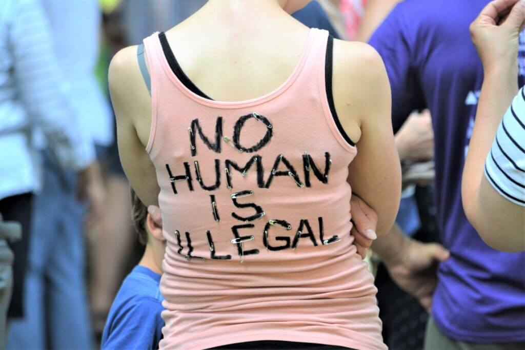 Mujer de espaldas con una inscripción en la remera que dice "Ningún humano es ilegal"
