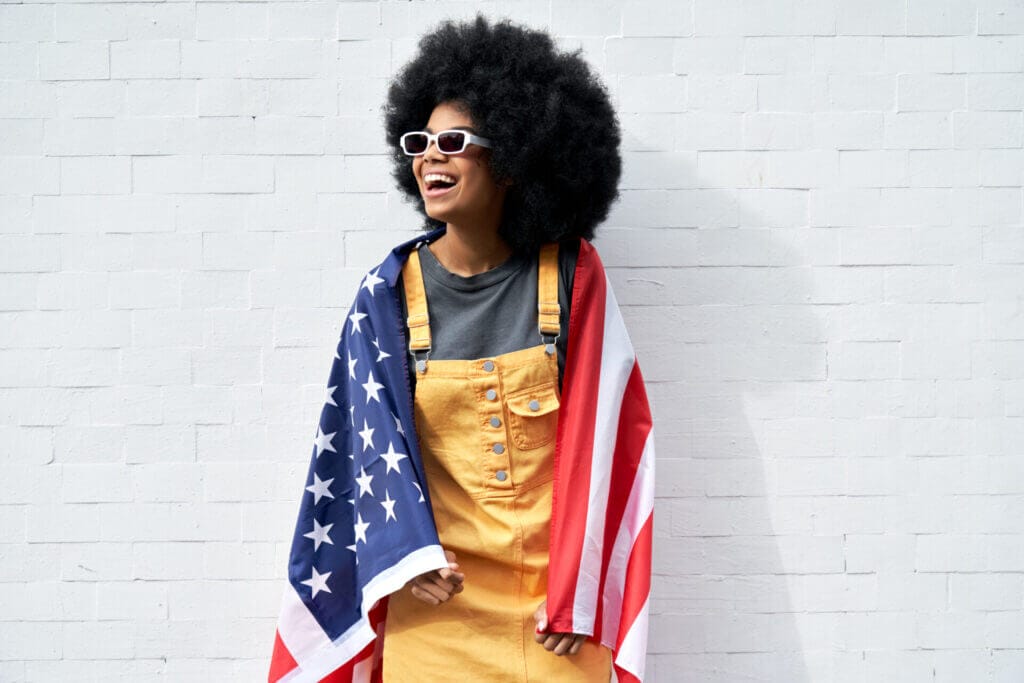Joven afroamericana envuelta en la bandera estadounidense sonriendo. 