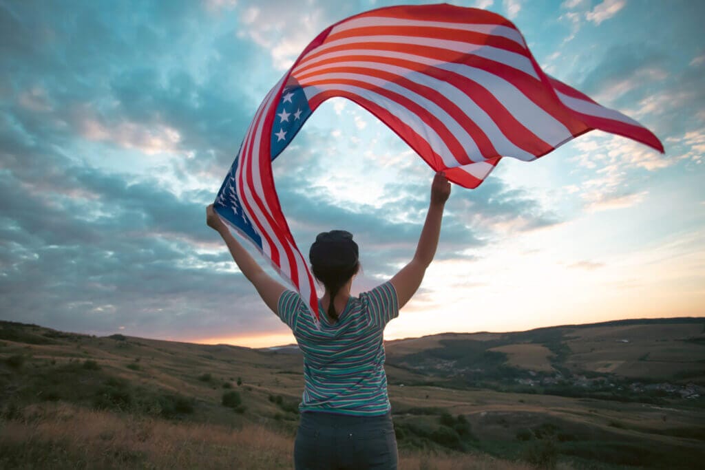 Joven migrante con bandera de USA flameando en sus manos