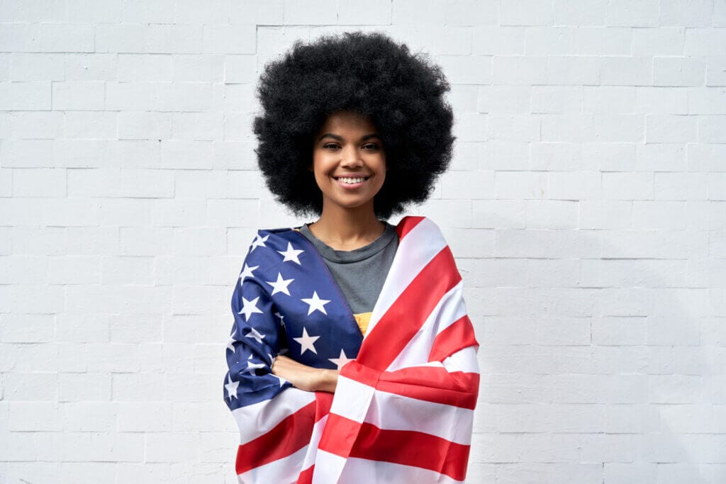 Mujer afrolatina envuelta en una bandera estadounidense sonriendo a la cámara