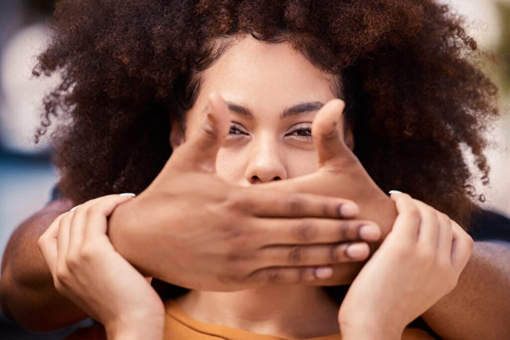 Mujer morena con manos tapandole la boca simbolizando los peligros de callar cuando se es víctima de violencia u otros delitos.