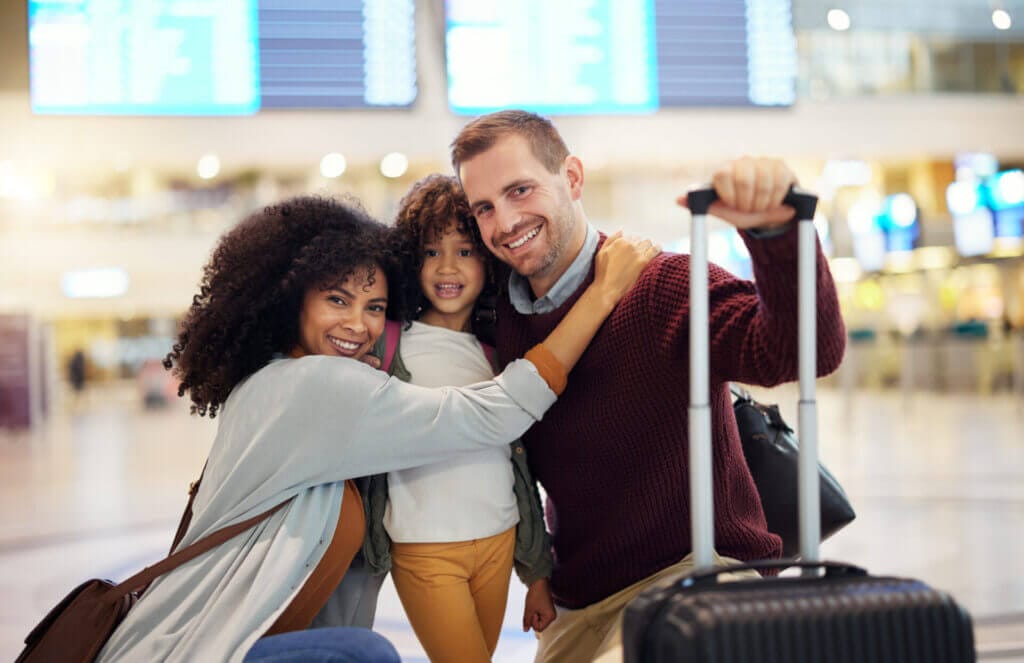 Familia de migrantes en el aeropuerto, sonriendo a la cámara con sus valijas