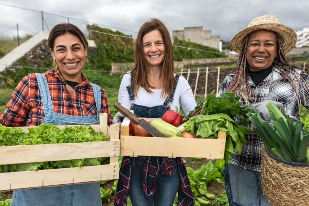 Trabajadoras latinas agrícolas sonriendo a la cámara con cajones de productos