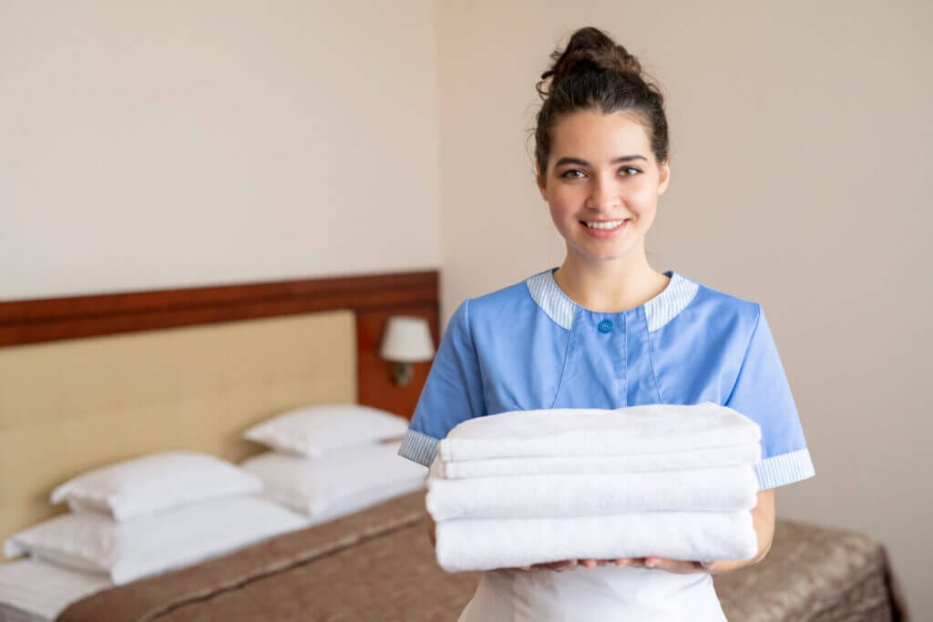 Empleada doméstica en uniforme sosteniendo toallas y sonriendo a la cámara.