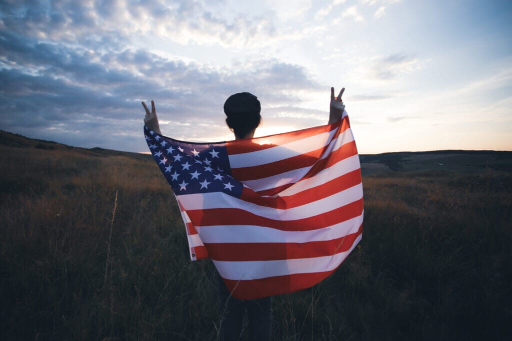Mujer de espaldas a un paisaje con la bandera de Estados Unidos a sus hombros