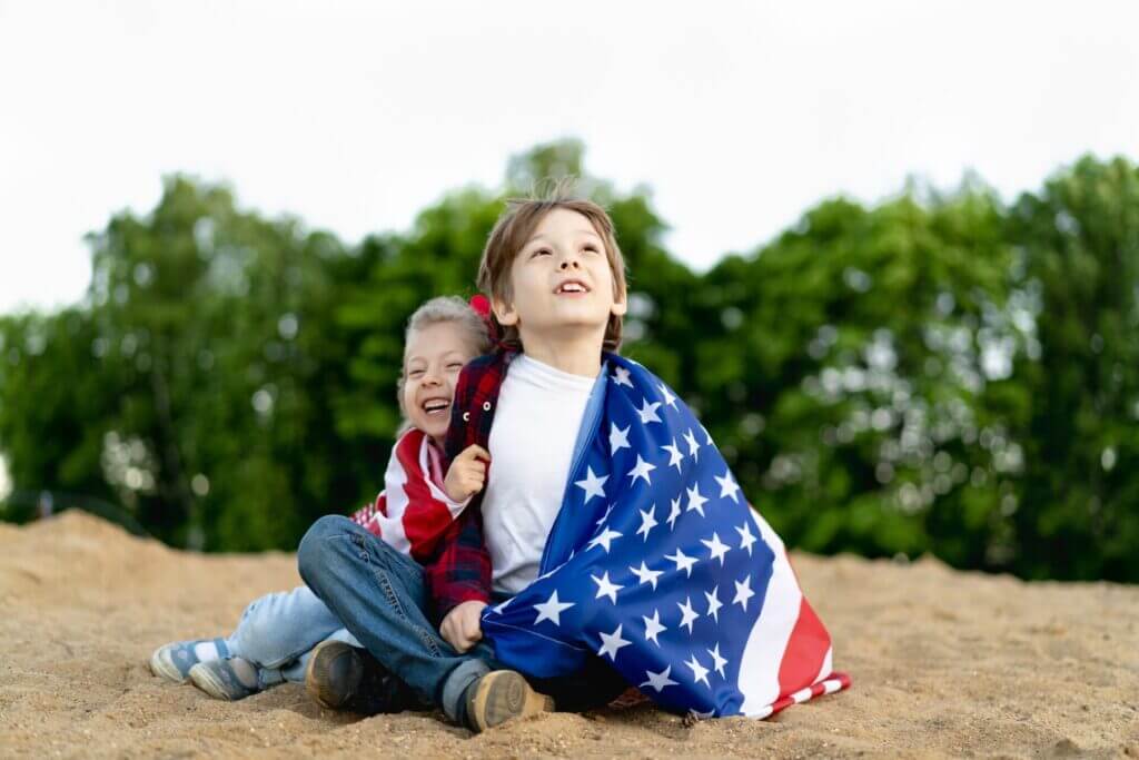 Hermano y hermana mirando al cielo con la bandera estadounidense rodeando sus hombros.