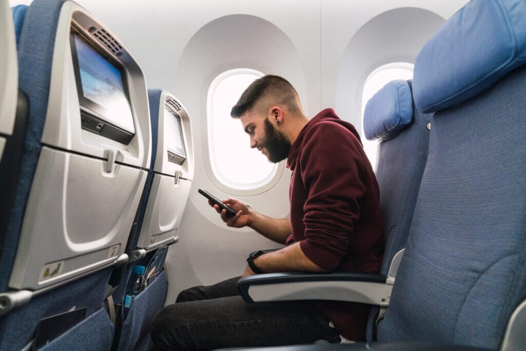 Hombre sentado en un avión mirando su celular
