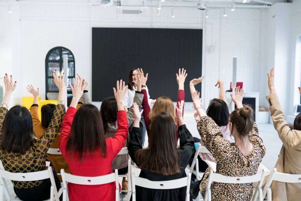 Grupo de personas sentadas levantando la mano en una clase de inglés