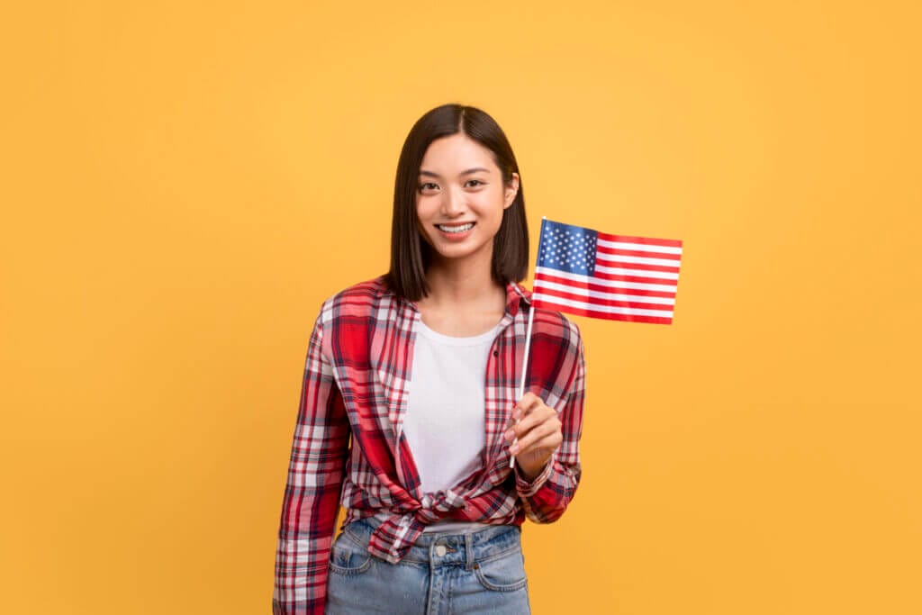Mujer migrante sonriendo a la cámara con una bandera de USA tras haber recibido su ciudadanía
