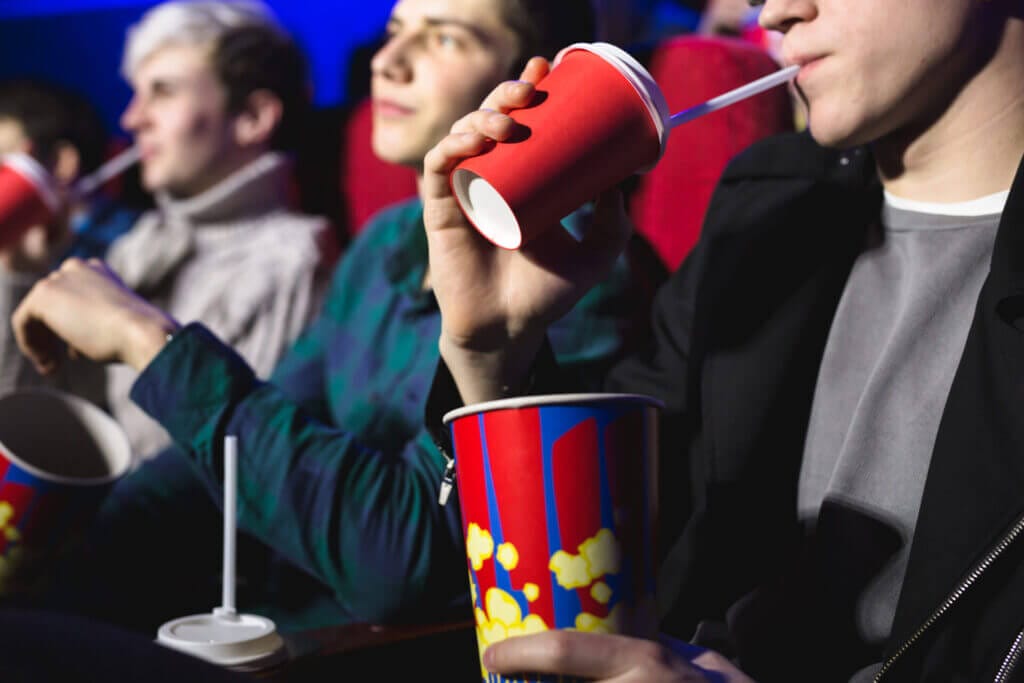 Grupo de amigos en el cine tomando bebidas y comiendo pochoclos mientras miran la película