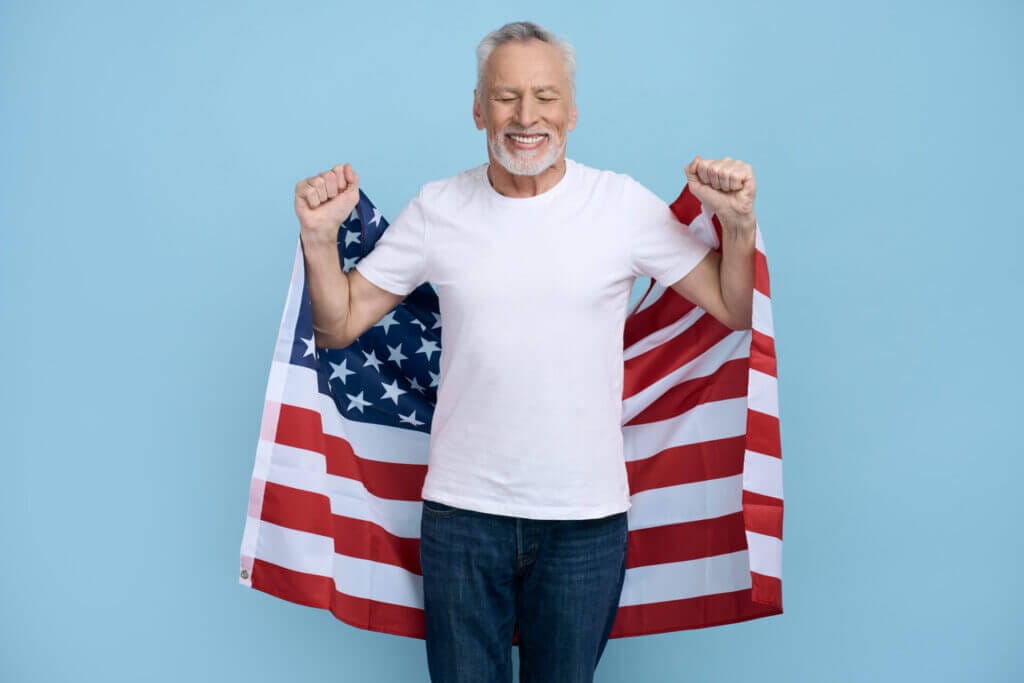 Retrato de un hombre mayor sonriendo con una bandera americana detrás  