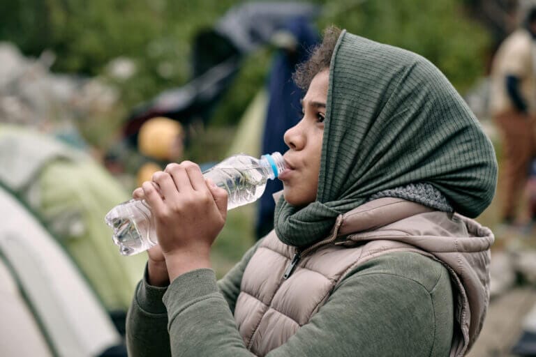 Joven migrante tomando agua en un campamento de refugiados tras aprender como pedir refugio en estados unidos con su familia