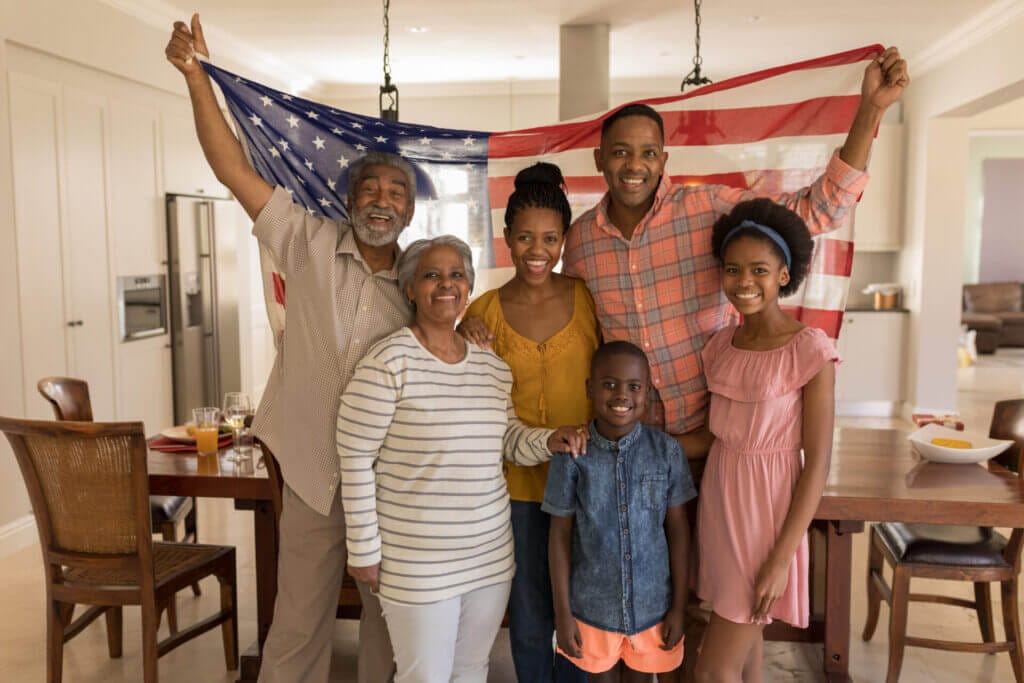 Familia de inmigrantes sonriendo frente a la cámara sosteniendo una bandera americana