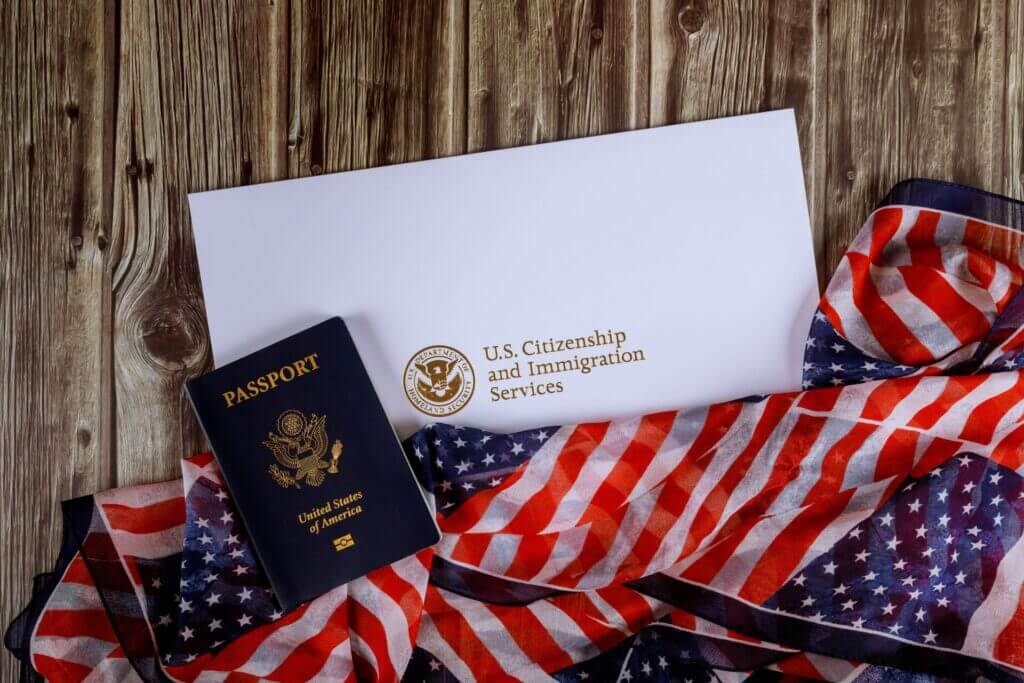 Pasaporte de USA junto a la bandera y un documento de ciudadanía representando la ayuda para aplicar para la ciudadania