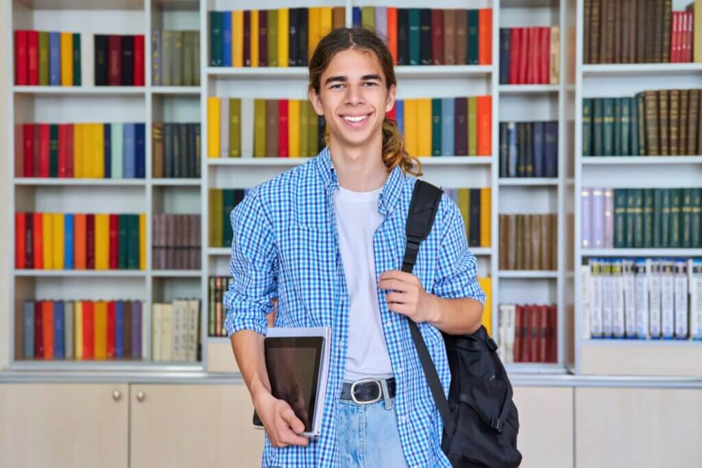 Retrato de un adolescente en la librería de su colegio sonriendo a la cámara
