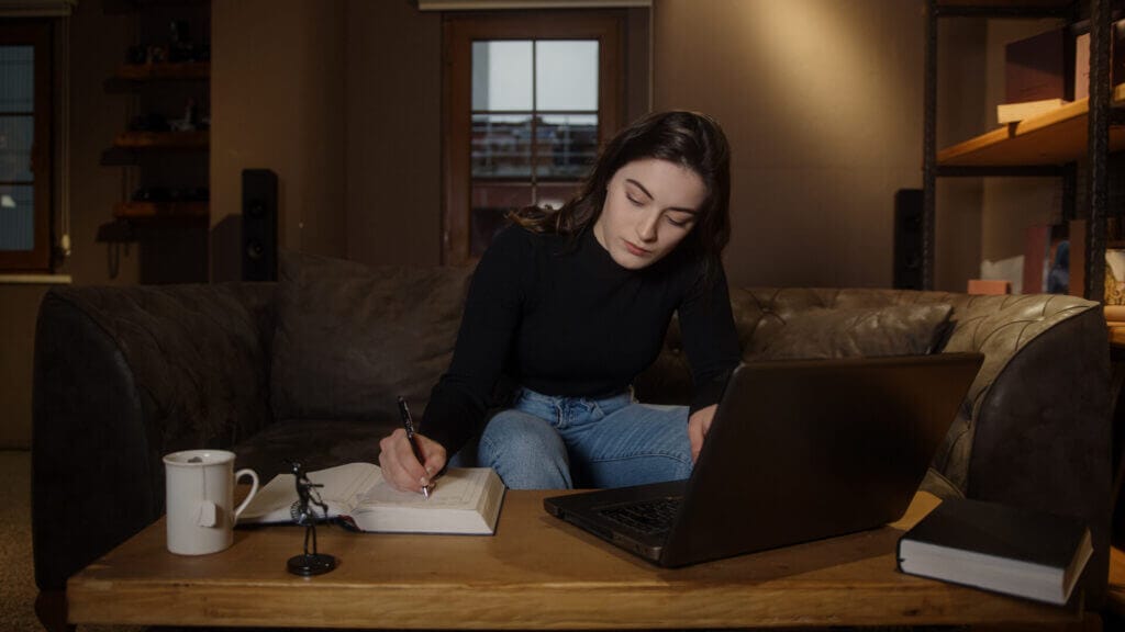 Joven mujer en su sofá revisando documentos migratorios en su laptop