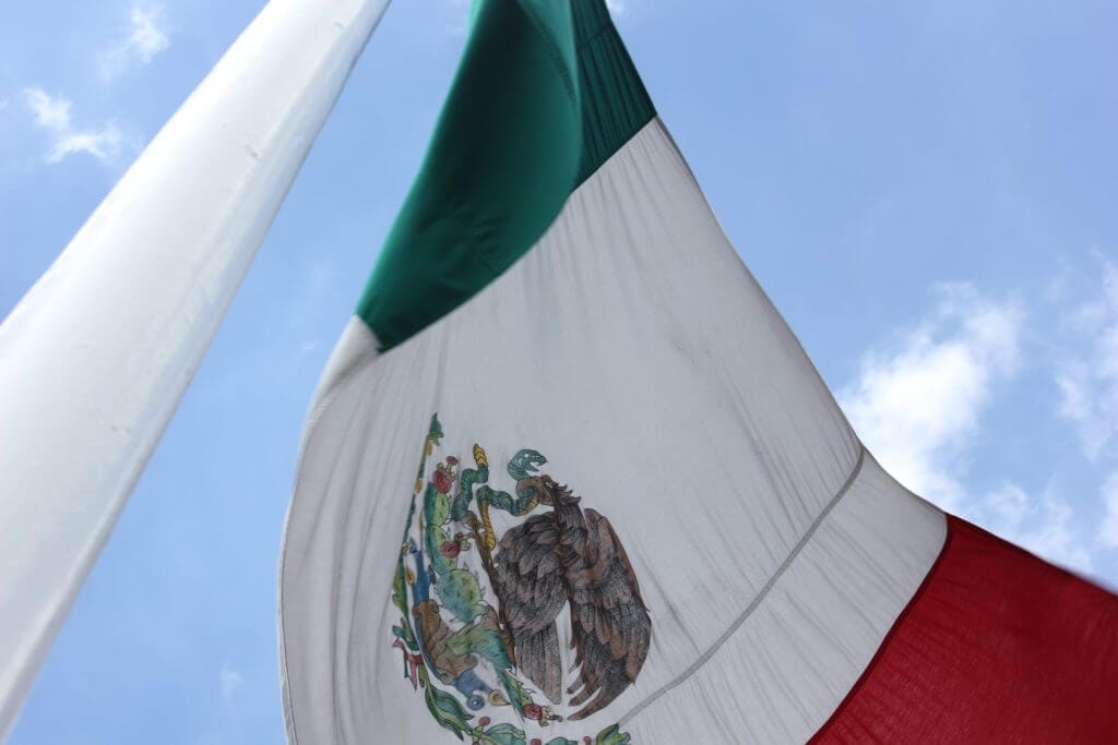 Imagen de cerca de la bandera de México flameante de un poste representando la crisis fronteriza que azota la nación