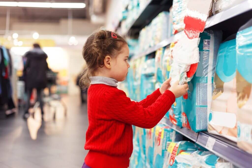 Niña pequeña en el supermercado viendo pañales gracias a las tarjetas de credito para inmigrantes