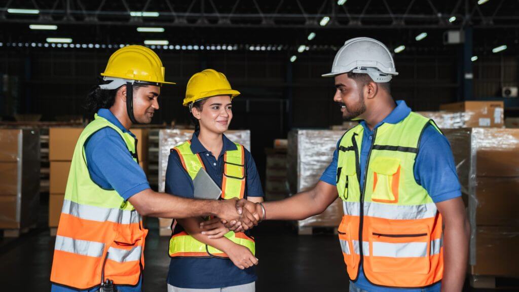 Tres trabajadores de fábrica estrechandose la mano y sonriendo