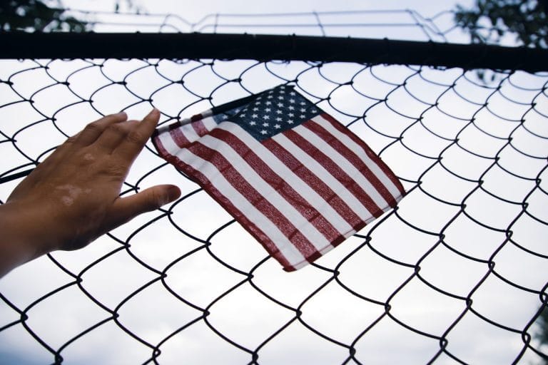 Mano con una bandera de USA sobre una reja representando la amnistía en Estados Unidos