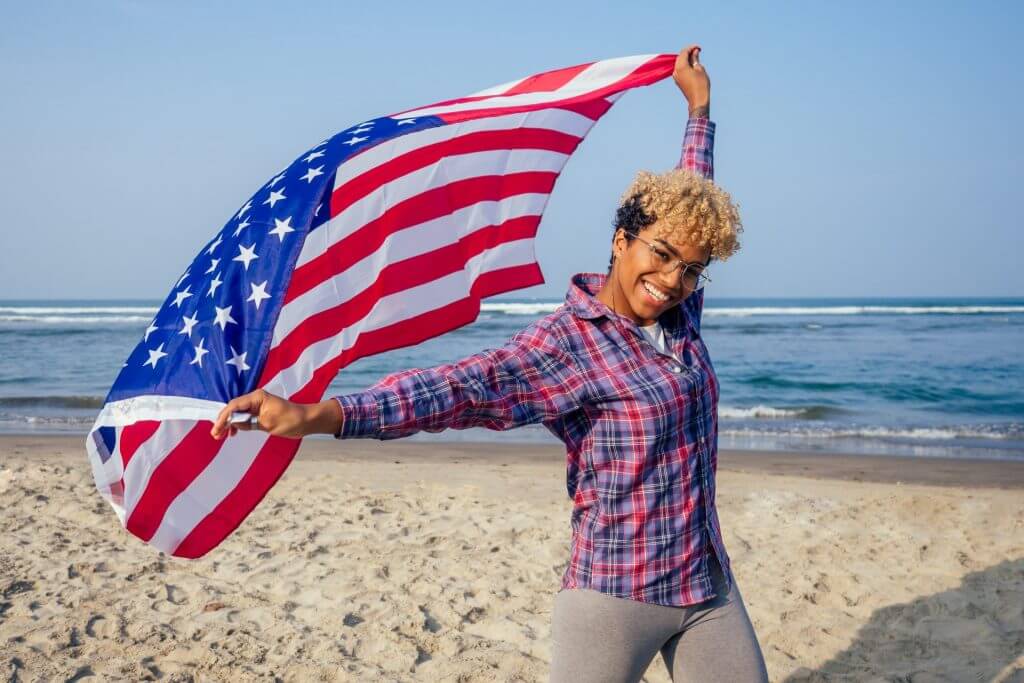 Mujer feliz en la playa con una bandera de USA