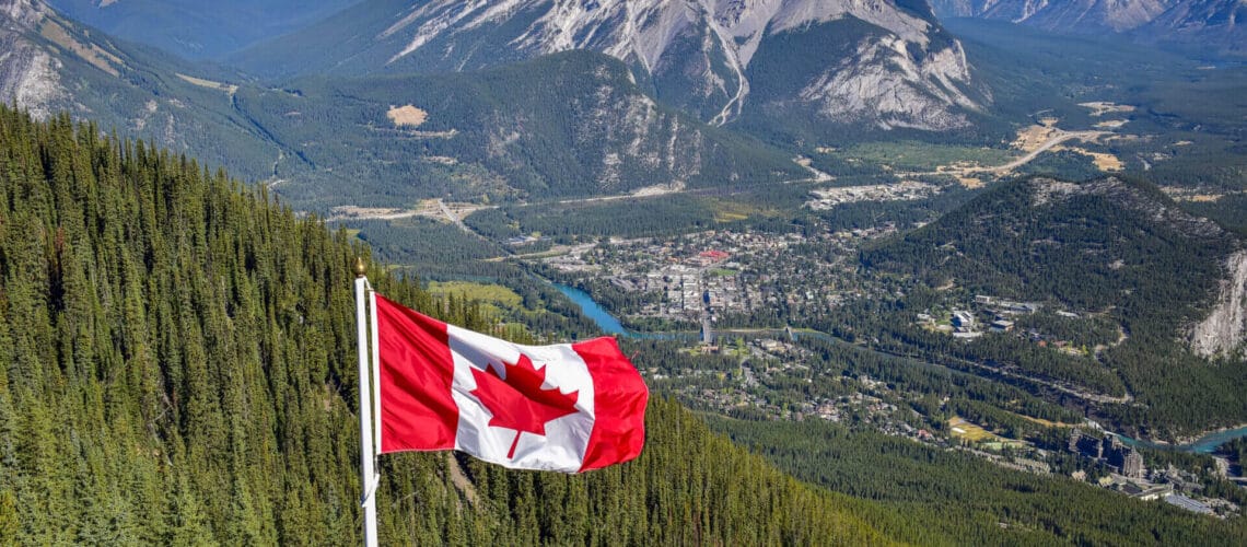 Bandera de Canadá ondeando sobre las Montañas Rocosas. Este artículo habla sobre emigrar a Canadá.