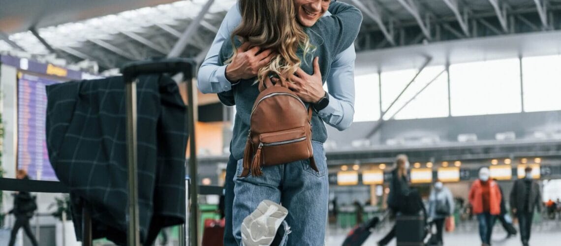 Joven pareja se abraza en aeropuerto.