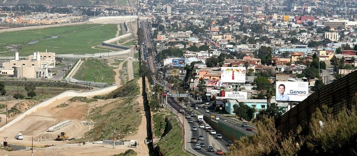 Este artículo habla sobre Quédate en México. La imagen muestra la frontera de México y Estados Unidos desde un punto elevado del camino fronterizo.