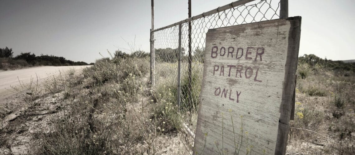 Muro de reja en la frontera entre Estados Unidos y México. Un cartel de madera indica que el camino es exclusivo para la Patrulla Fronteriza.
