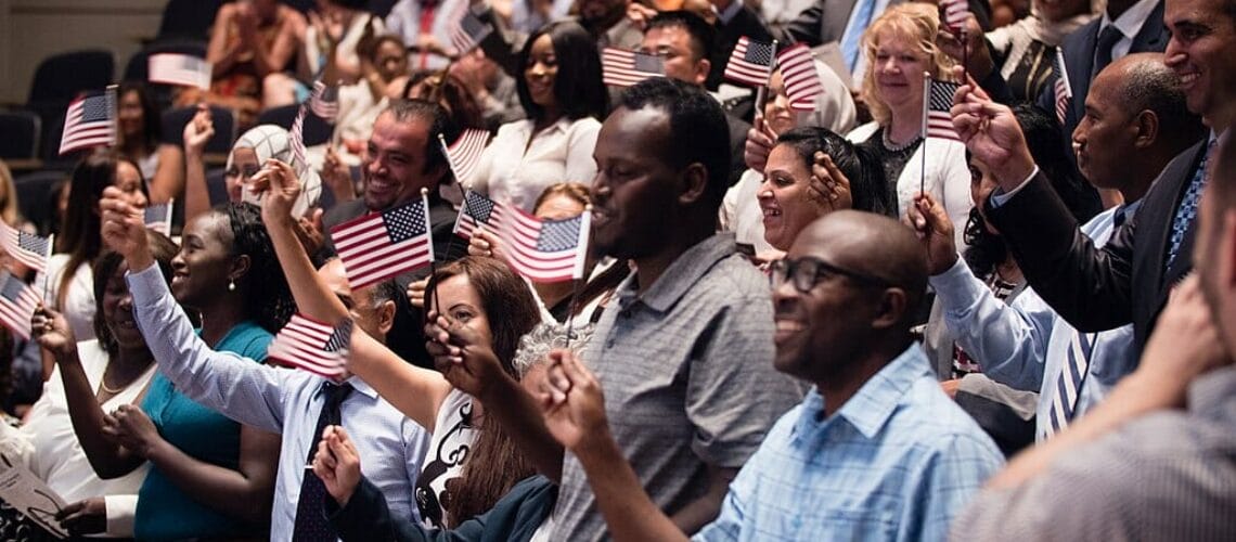 Este artículo habla sobre la nueva regla de carga pública. La foto muestra muchas personas con banderines de los Estados Unidos.