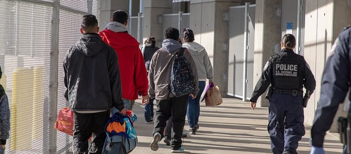 Grupo de migrantes vistos de espalda haciendo fila para solicitar asilo. Los neuvos programas de parole humanitario buscan reducir la cantidad de tráfico humano en la frontera y generar nuevas vías migratorias.