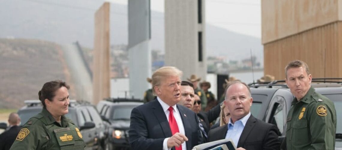 Este artículo habla sobre la separación de familias migrantes. La imagen muestra al ex presidente Donald Trump en la frontera observando prototipos para el muro fronterizo.