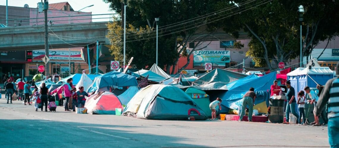 Este artículo habla sobre los migrantes que aguardan del lado mexicano para cruzar la frontera. La imagen muestra un campamento de migrantes en Tijuana.